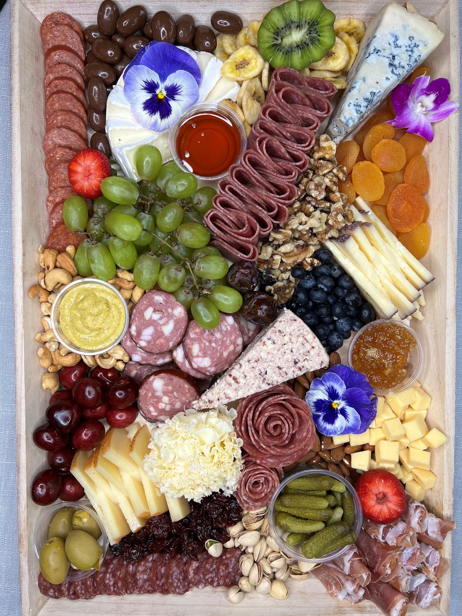 Rectangular charcuterie board with brie, kiwi, honey, and cured meats