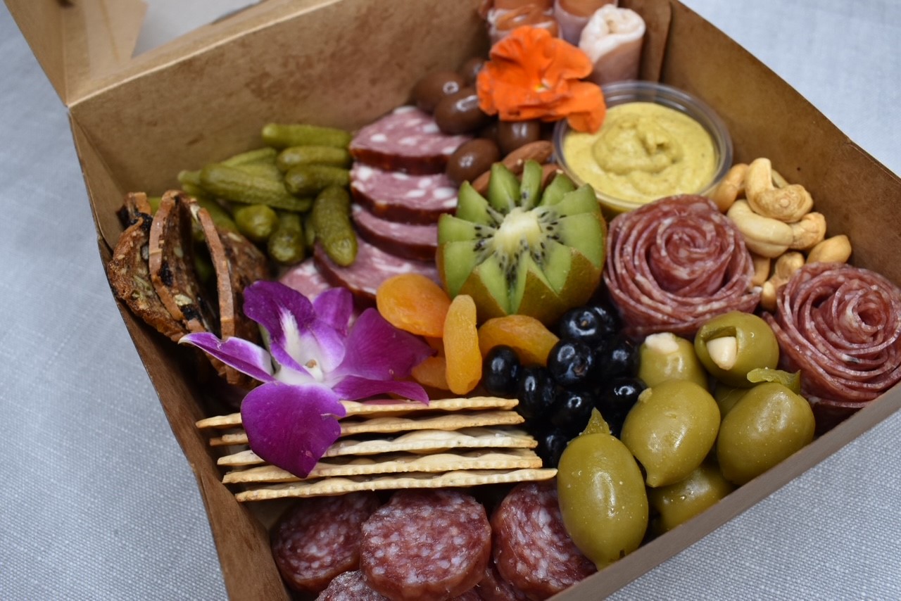 Boxed charcuterie with olives, crackers, orchid, and salami