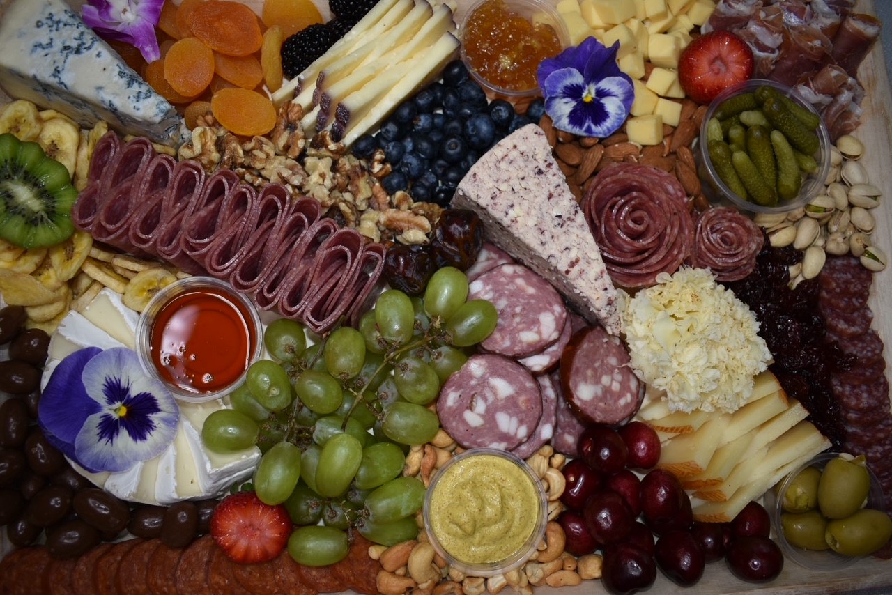 Overhead charcuterie board with pansies, blueberries, and artisan cheeses