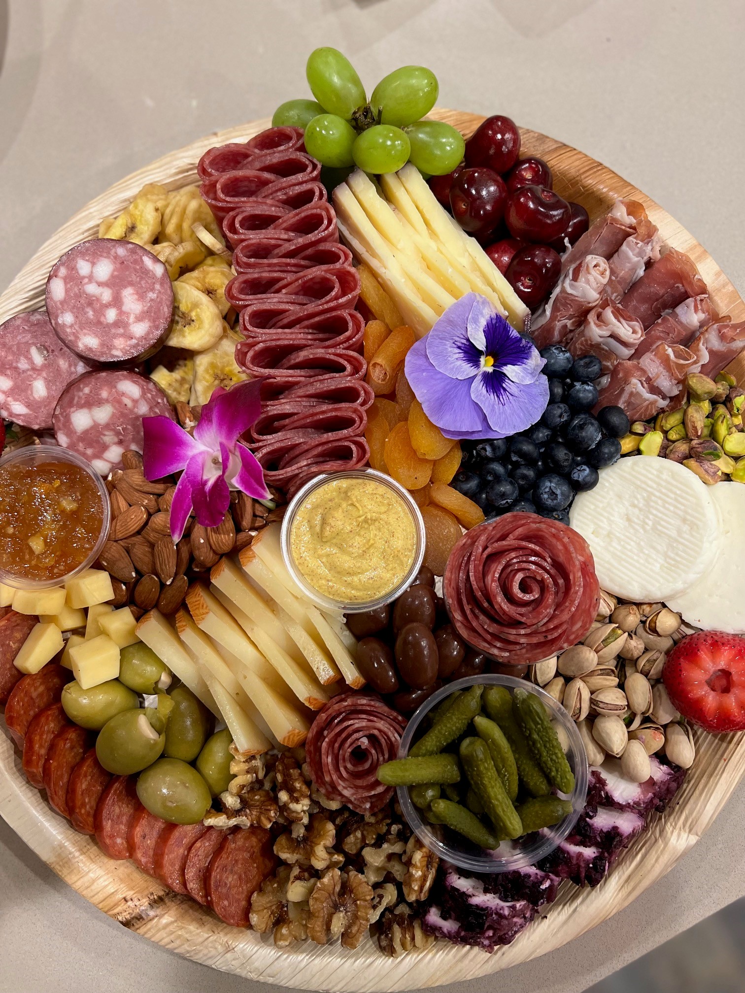 Round charcuterie board with grapes, almonds, mustard, and salami roses